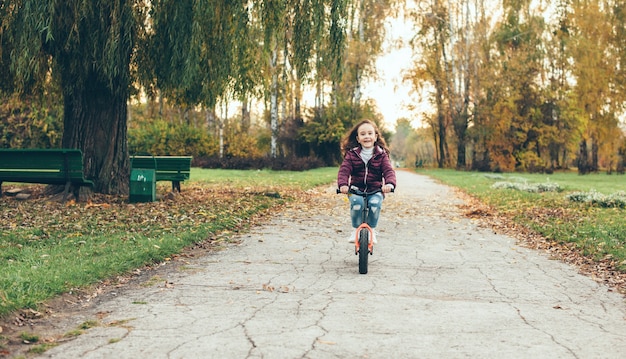 Bella piccola ragazza in bicicletta che cammina da solo nel parco in una giornata autunnale