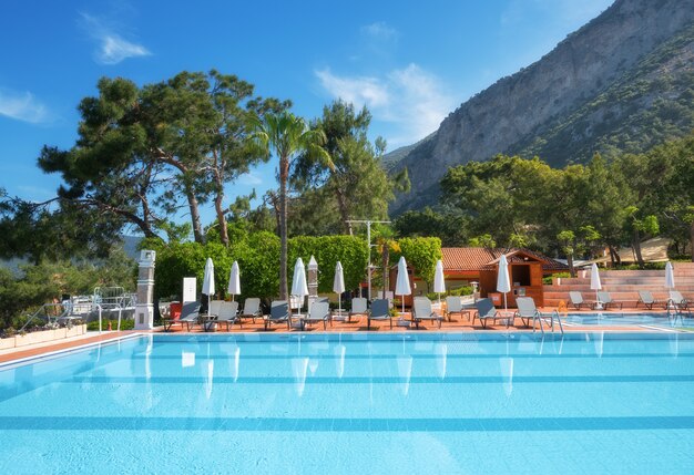 Bella piscina con lettini e ombrelloni all'alba in estate. Resort di lusso. Hotel Liberty Lykia. Oludeniz, Turchia. Paesaggio con piscina vuota, sedie a sdraio, alberi verdi, montagna, cielo blu