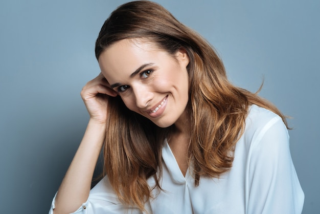 Bella posa. Gioiosa bella donna positiva che sorride e ti guarda mentre si tiene i capelli