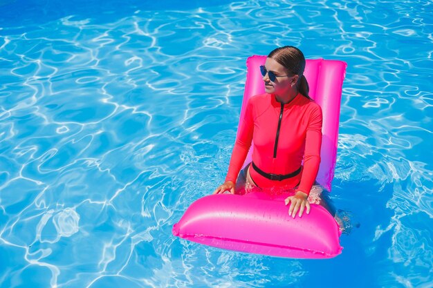 Bella ragazza abbronzata in costume da bagno rosa e occhiali a bordo piscina Tiene un materasso ad aria rosa occhiali da sole pelle abbronzata bagnata Spiaggia del resort per le vacanze Giornata di sole