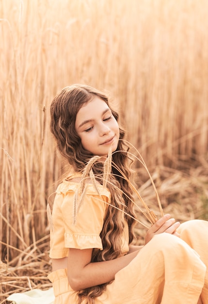 Bella ragazza adolescente con i capelli lunghi che cammina attraverso un campo di grano in una giornata di sole. Ritratto all'aperto. Studentessa rilassante