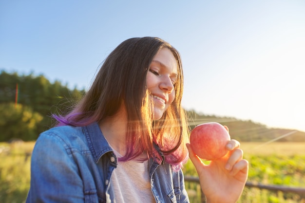 Bella ragazza adolescente con mela rossa, giovane donna felice sulla natura, sfondo panoramico del paesaggio al tramonto, spazio copia, concetto di cibo naturale sano