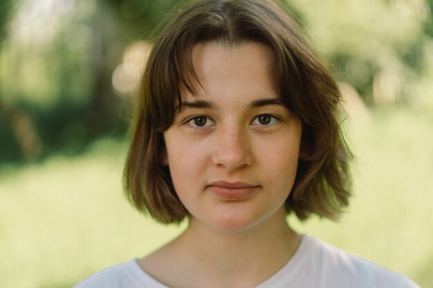 Bella ragazza adolescente con un taglio di capelli alla moda in una maglietta bianca all'aperto e guardando c...