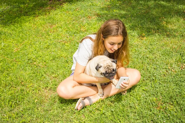 Bella ragazza adolescente guardando un video divertente su uno smartphone con il suo cane in un parco di estate