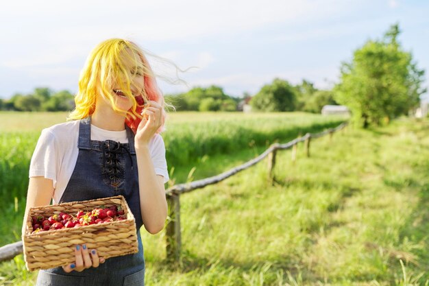 Bella ragazza adolescente sorridente in fattoria rustica con cesto di fragole fresche copia spazio sul paesaggio naturale estivo di erba verde