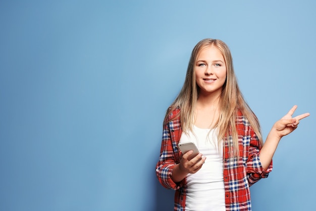 Bella ragazza adolescente utilizzando smart phone sulla parete blu