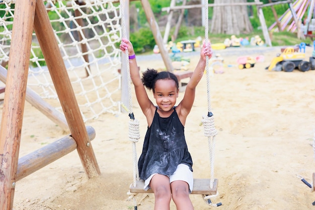 Bella ragazza africana gioca swing nell'apprendimento del campo estivo del parco giochi