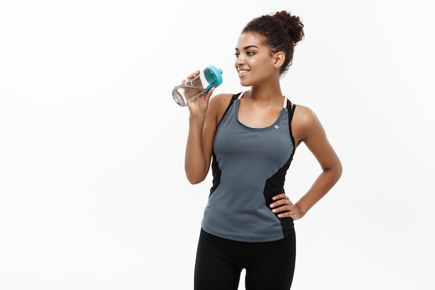 bella ragazza afroamericana in abiti sportivi azienda bottiglia di acqua dopo allenamento.