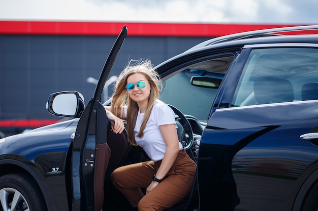 Bella ragazza alla moda alla moda che si siede nel salone di un'auto di classe business nera. Giovane donna con un sorriso sul viso.