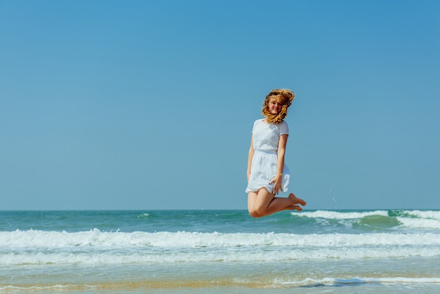 Bella ragazza allegra che salta sulla spiaggia