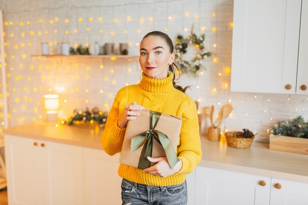 Bella ragazza allegra felice con i regali di Natale sulla cucina del nuovo anno