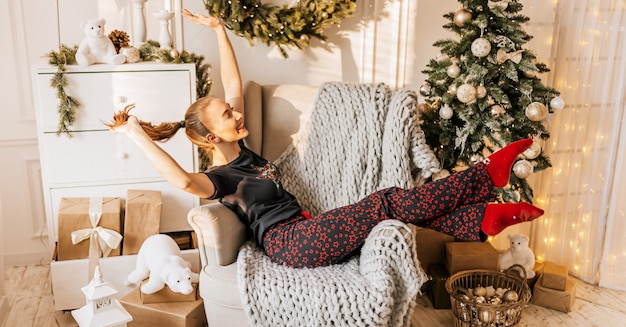 Bella ragazza allegra felice in pigiama con i regali di Natale sul divano sullo sfondo di un albero di Capodanno a casa