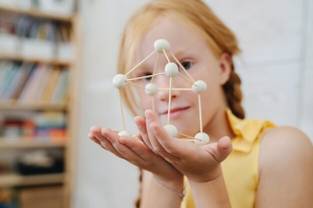 Bella ragazza allo zenzero che presenta la forma a d che ha fatto con la plastilina e gli stuzzicadenti