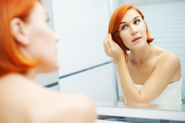 Bella ragazza applica cosmetici sul viso in bagno leggero.