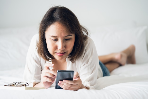 Bella ragazza asiatica che dorme su uno smartphone. Gioca sui media.