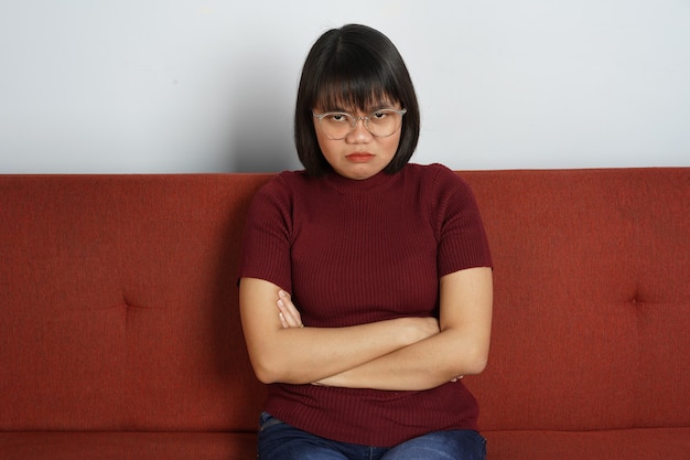 Bella ragazza asiatica che indossa una camicia rossa e jeans blu Seduta sul divano rosso e si arrabbia con un gesto