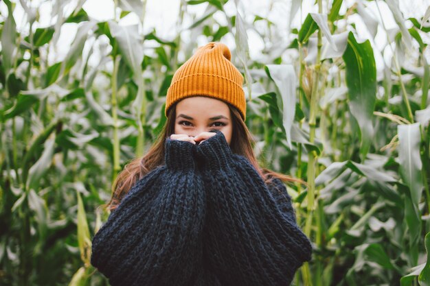 Bella ragazza asiatica che porta cappello giallo e maglione tricottato nel campo di grano di autunno.