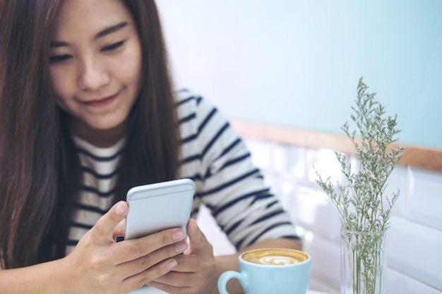 Bella ragazza asiatica con faccina holding e utilizzando il telefono intelligente nel moderno colore pastello