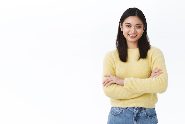 Bella ragazza asiatica con i capelli corti in piedi su sfondo bianco con espressione sicura pronta guardando la fotocamera e sorridente felice mostrando professionalità studente alla ricerca di opportunità di carriera