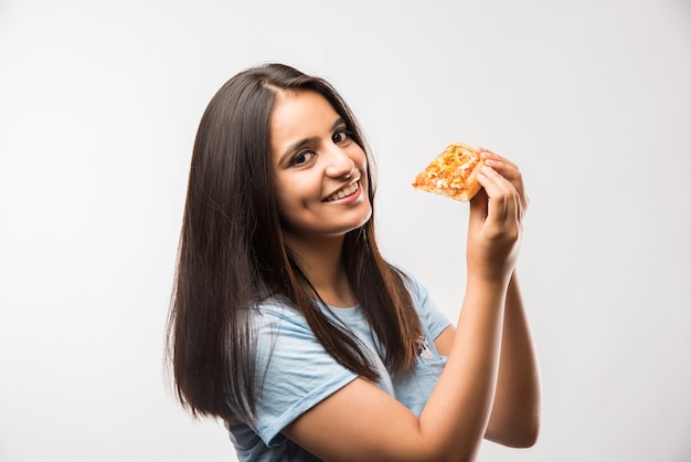 Bella ragazza asiatica indiana che mangia una fetta di pizza in piedi isolata su sfondo bianco