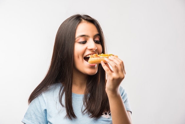 Bella ragazza asiatica indiana che mangia una fetta di pizza in piedi isolata su sfondo bianco