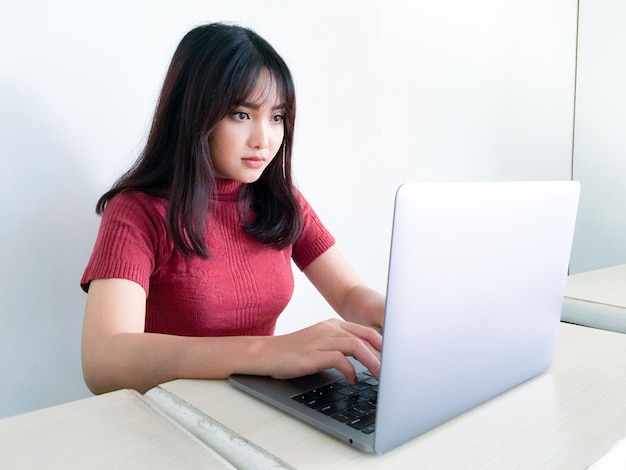 Bella ragazza asiatica seria o pensando nella parte anteriore del computer portatile sullo sfondo bianco isolato