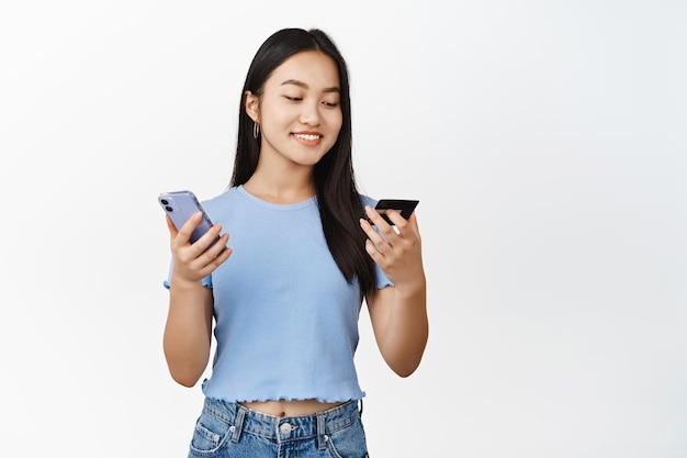 Bella ragazza asiatica sorridente utilizzando la carta di credito e l'ordine del telefono cellulare su smartphone pagando sfondo bianco contactless