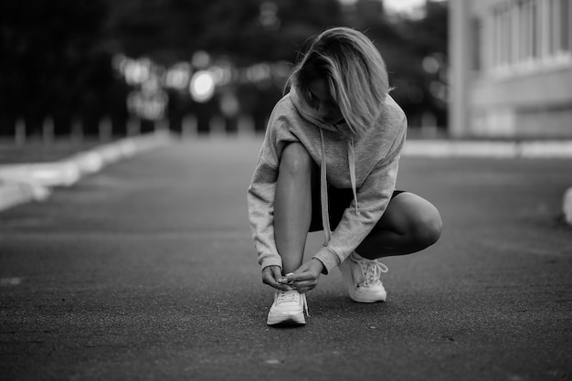 bella ragazza atleta seduta legatura lacci delle scarpe su scarpe da ginnastica bianche foto in bianco e nero