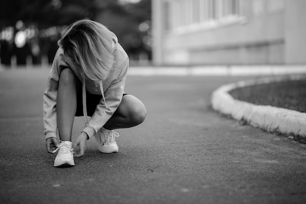 bella ragazza atleta seduta legatura lacci delle scarpe su scarpe da ginnastica bianche foto in bianco e nero