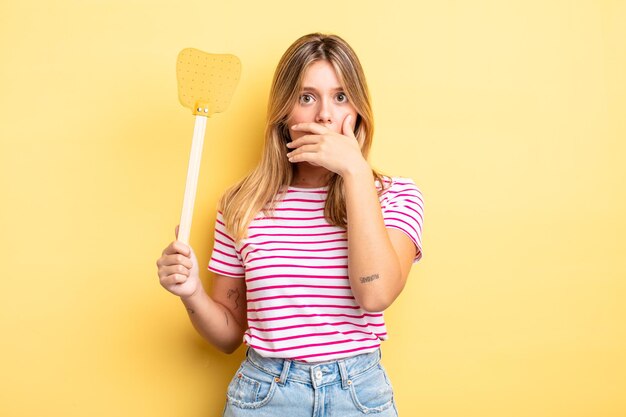 Bella ragazza bionda che copre la bocca con le mani con uno scioccato. uccidere mosche concetto