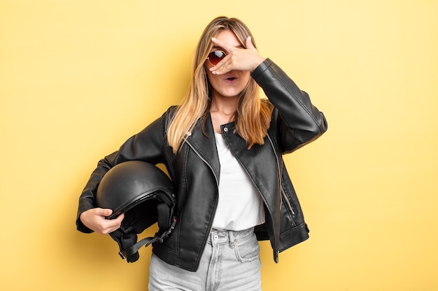 bella ragazza bionda che sembra scioccata, spaventata o terrorizzata, coprendo il viso con la mano. concetto di casco da moto