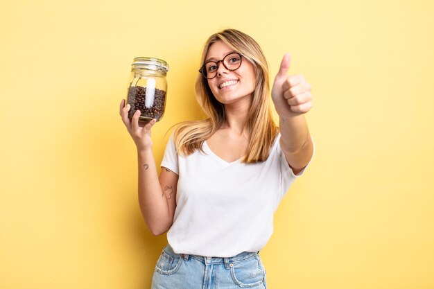 Bella ragazza bionda che si sente orgogliosa, sorride positivamente con i pollici in su. concetto di chicchi di caffè