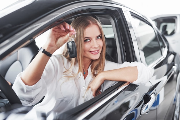 Bella ragazza bionda che si siede nella nuova automobile con interni neri moderni