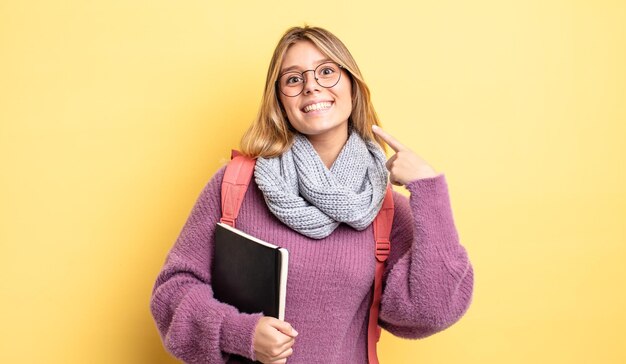 Bella ragazza bionda che sorride con sicurezza indicando il proprio ampio sorriso. concetto di studente