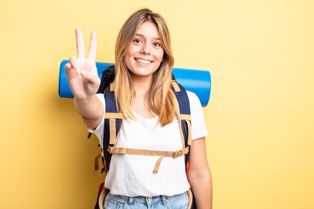 Bella ragazza bionda che sorride e sembra felice, gesticolando vittoria o pace. concetto di escursionista