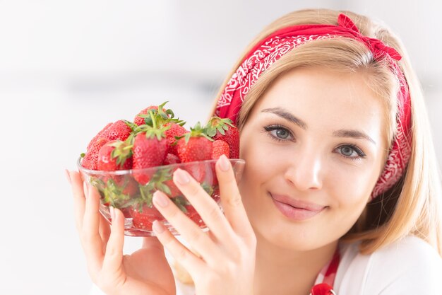 Bella ragazza bionda che tiene una ciotola di fragole accanto al viso.