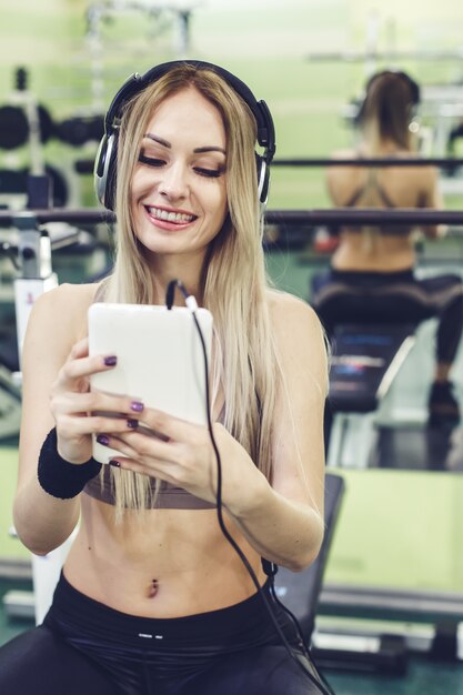 Bella ragazza bionda che utilizza un PC della compressa, preparantesi in una palestra.