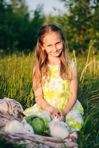 bella ragazza bionda con coniglietti seduto sull'erba verde. y