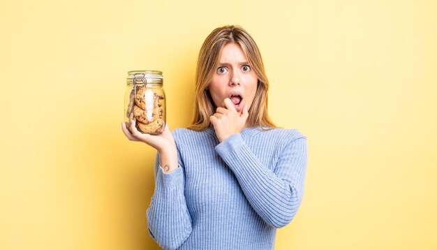 Bella ragazza bionda con la bocca e gli occhi spalancati e la mano sul mento. concetto di biscotti fatti in casa