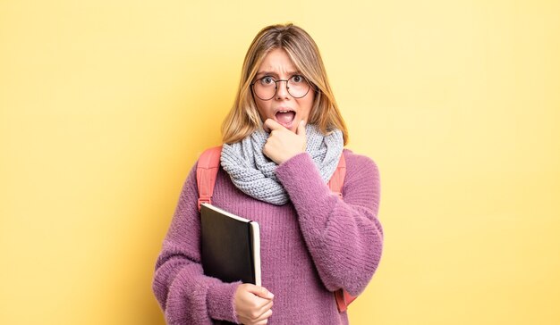 bella ragazza bionda con la bocca e gli occhi spalancati e la mano sul mento. concetto di studente