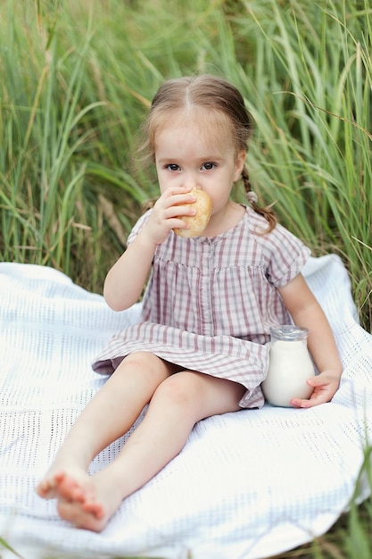 Bella ragazza bionda di 3 anni con un vestito marrone in un campo di grano con una brocca di latte, vita di villaggio.