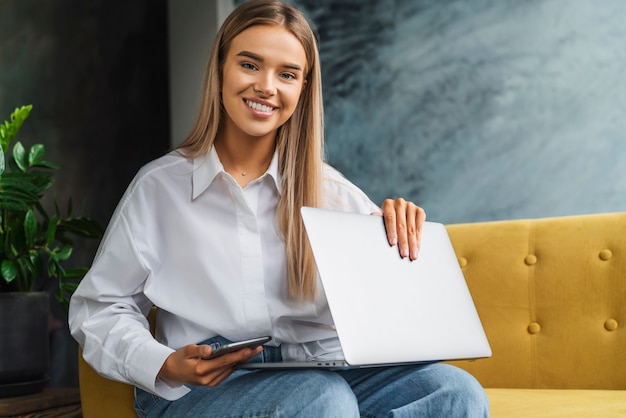 Bella ragazza bionda freelance sta facendo progetto da casa, utilizzando dispositivi collegati, accesso a Internet