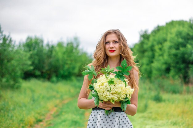 bella ragazza bionda giovane ha raccolto un mazzo di fiori di campo. Goditi una passeggiata in una calda giornata estiva