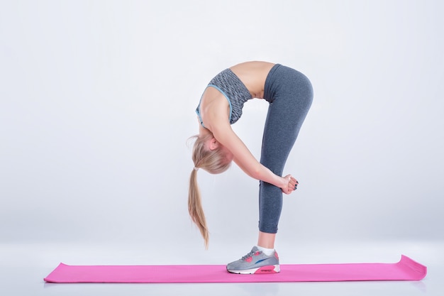 bella ragazza bionda in abbigliamento sportivo fa esercizi su un tappetino fitness su sfondo grigio