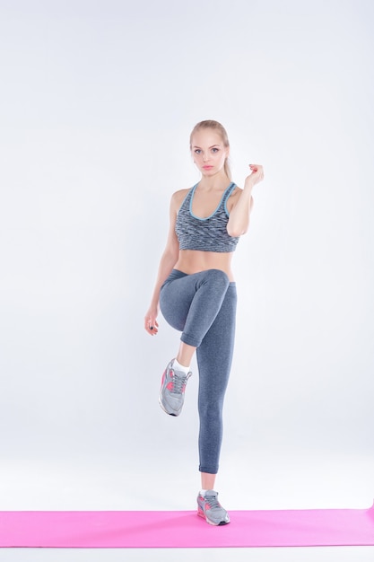 bella ragazza bionda in abbigliamento sportivo fa esercizi su un tappetino fitness su sfondo grigio