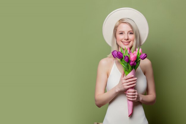 Bella ragazza bionda in cappello bianco e vestito con i tulipani