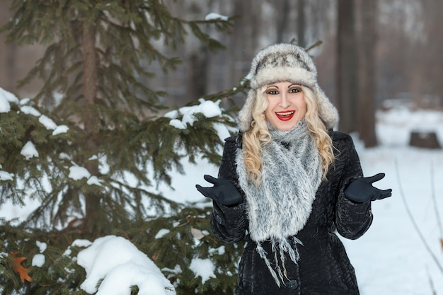 Bella ragazza bionda in piedi nella foresta di inverno vicino a un albero