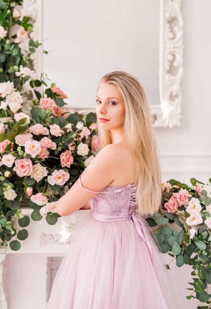 Bella ragazza bionda in un abito viola morbido lungo di fiori in posa. concetto di profumi, moda e bellezza