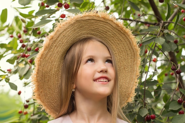 bella ragazza bionda in un cappello di paglia sullo sfondo di un ramo con ciliegie mature estate