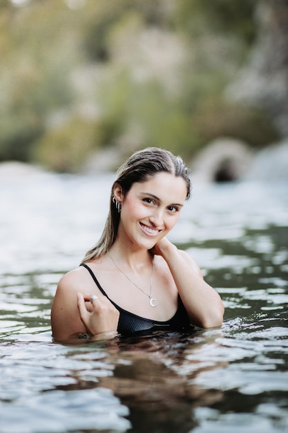 Bella ragazza bionda sorridente che esce dall'acqua in un fiume freddo. Verticale